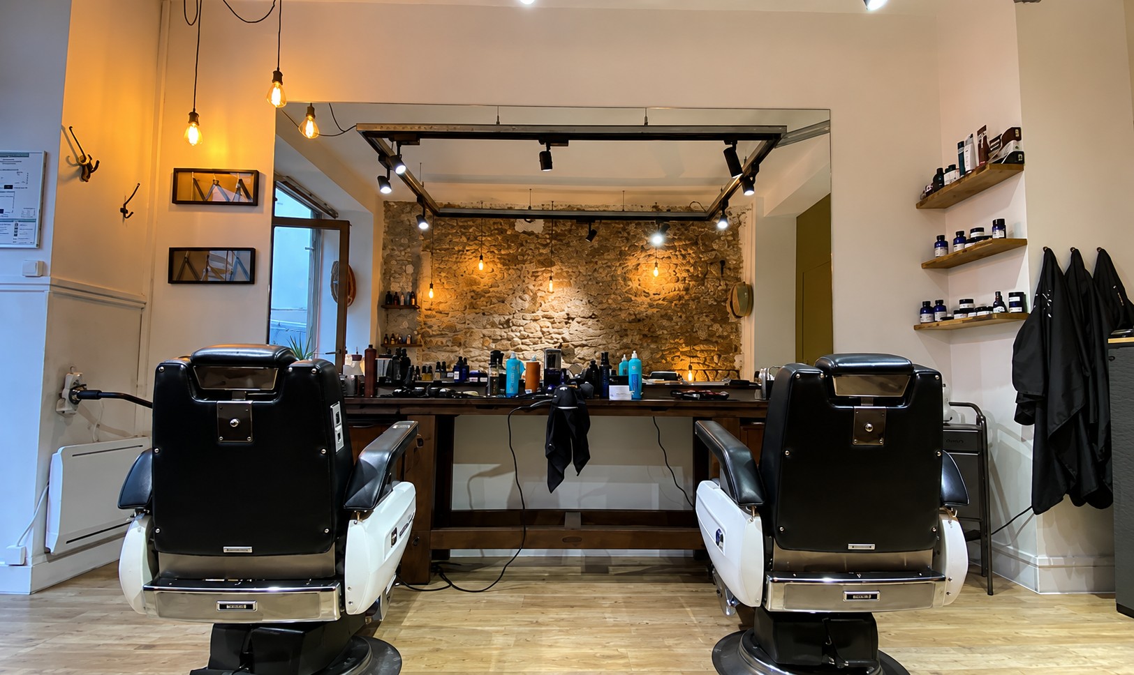 Intérieur du salon Raphaël : deux fauteuils de barbier face au mur de pierre et au plan de travail en bois